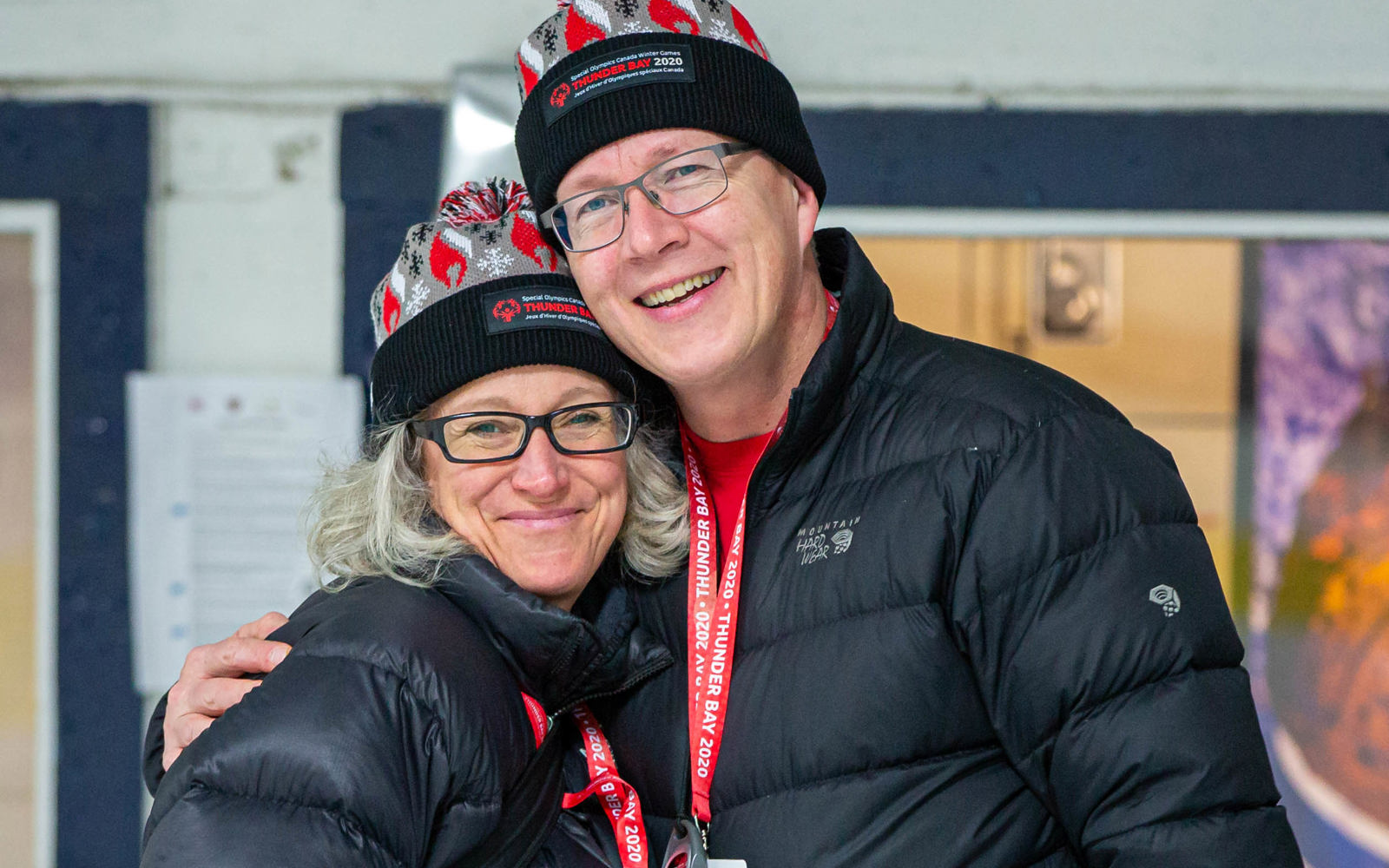 Two people in black winter jackets and Thunder Bay 2020 toques smile at the camera 